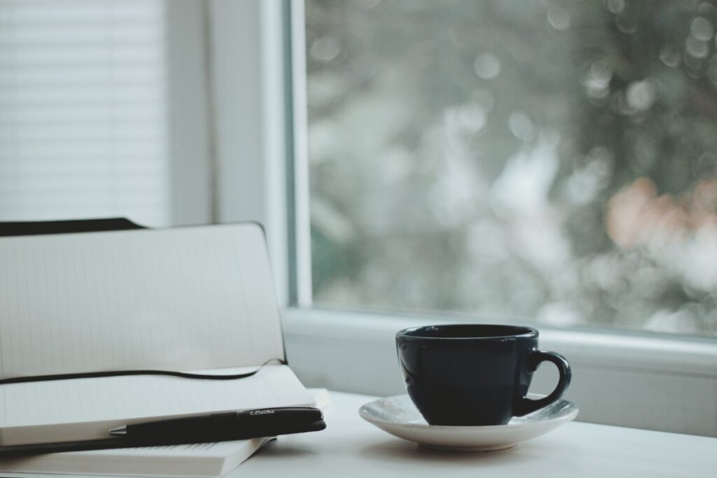 Notizbuch und Tasse auf einem Tisch am Fenster